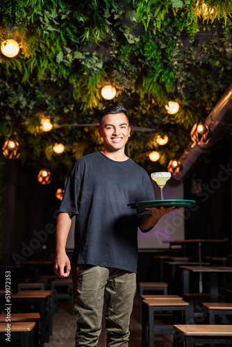 portrait of a waiter with a tray looking smiling at the camera in a nightclub