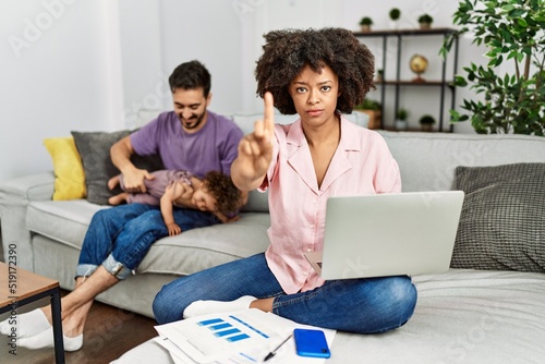 Mother of interracial family working using computer laptop at home pointing with finger up and angry expression, showing no gesture