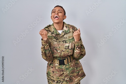 Beautiful african american woman wearing camouflage army uniform celebrating surprised and amazed for success with arms raised and eyes closed. winner concept.