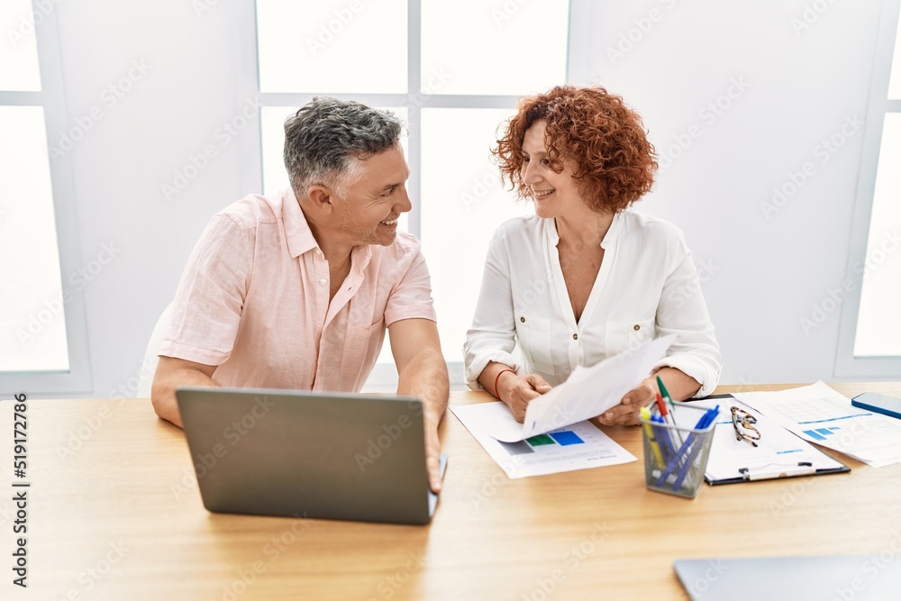 Middle age man and woman business workers using laptop and reading document at office Middle age man and woman business workers using laptop and reading document at office
