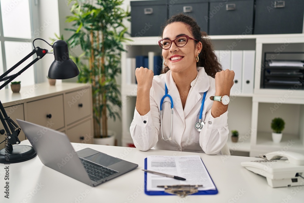 Young hispanic woman wearing doctor uniform and stethoscope celebrating surprised and amazed for success with arms raised and eyes closed. winner concept. Young hispanic woman wearing doctor uniform and stethoscope celebrating surprised and amazed for success with arms raised and eyes closed. winner concept.