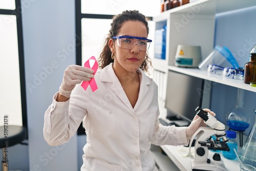 Young hispanic woman working at scientist laboratory looking for breast cancer cure skeptic and nervous  frowning upset because of problem. negative person.