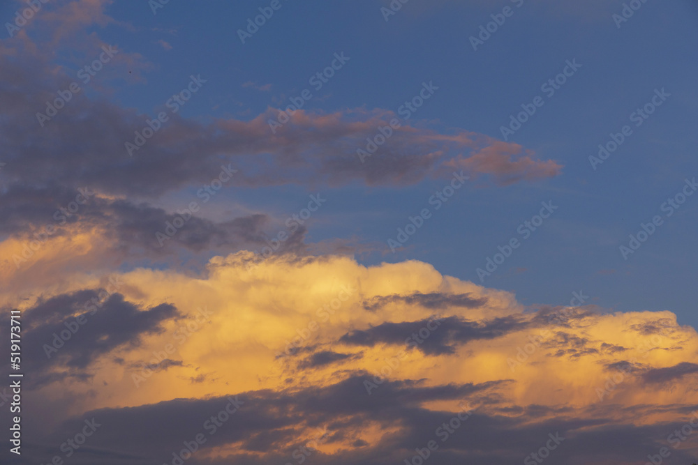 Golden and dark clouds on a sunset, dramatic evening blue sky background