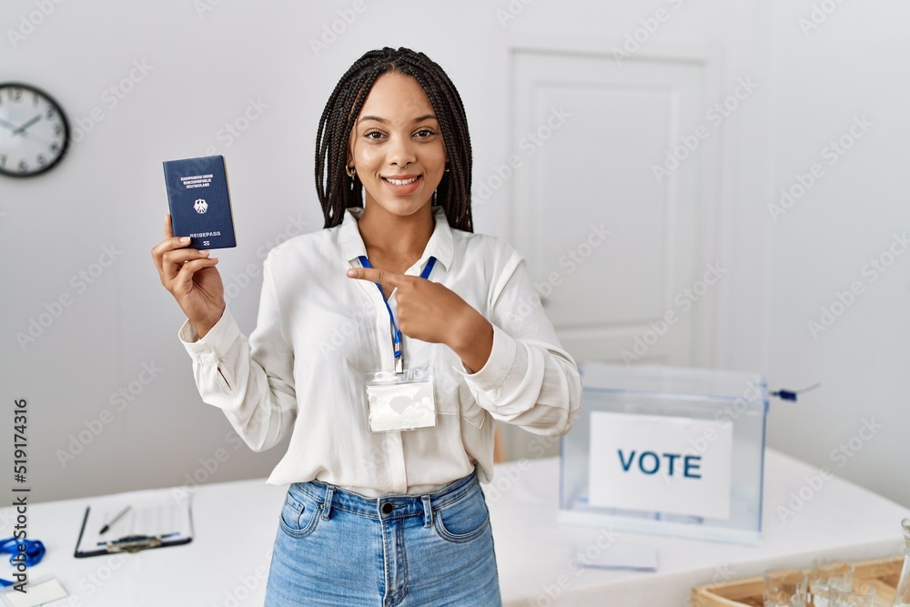 Young african american woman at political campaign election holding deutschland passport smiling happy pointing with hand and finger Young african american woman at political campaign election holding deutschland passport smiling happy pointing with hand and finger