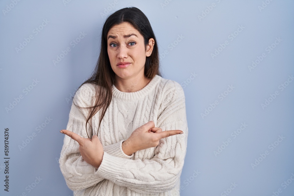 Young brunette woman standing over blue background pointing to both sides with fingers, different direction disagree Young brunette woman standing over blue background pointing to both sides with fingers, different direction disagree