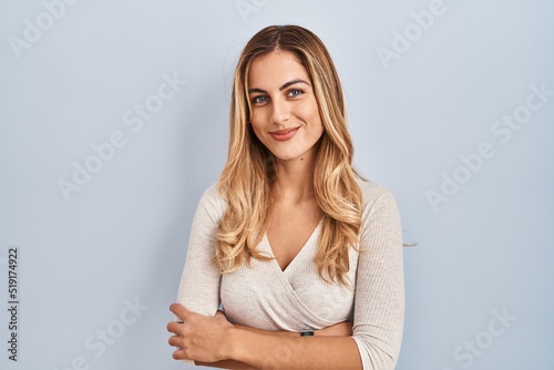 Young blonde woman standing over isolated background happy face smiling with crossed arms looking at the camera. positive person.