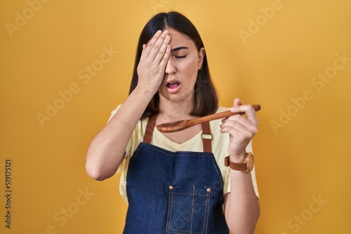 Hispanic girl eating healthy wooden spoon yawning tired covering half face, eye and mouth with hand. face hurts in pain.