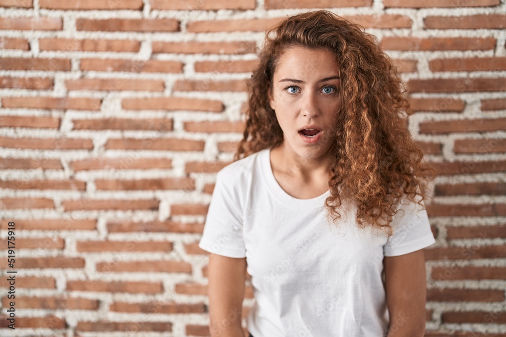 Young caucasian woman standing over bricks wall background afraid and shocked with surprise expression, fear and excited face. Young caucasian woman standing over bricks wall background afraid and shocked with surprise expression, fear and excited face.