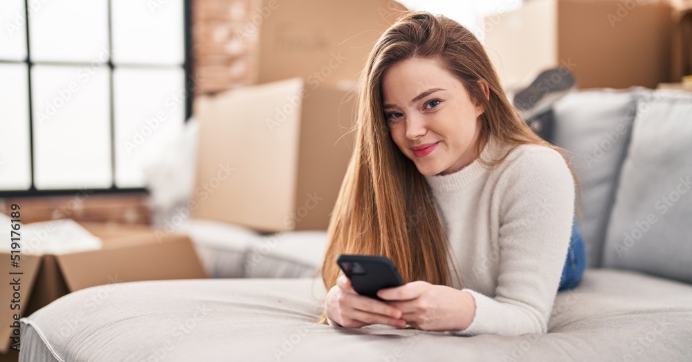 Young blonde woman using smartphone lying on sofa at new home Young blonde woman using smartphone lying on sofa at new home