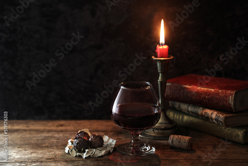 Obraz na płótnie Classic still life with vintage books and candle with a glass of red wine and chocolates at rustic dark background