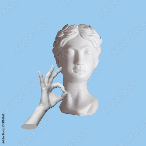 Antique female statue s head shows the ok gesture with hand isolated on a blue color background. Trendy abstact collage in magazine surreal style. 3d contemporary art. Modern design 