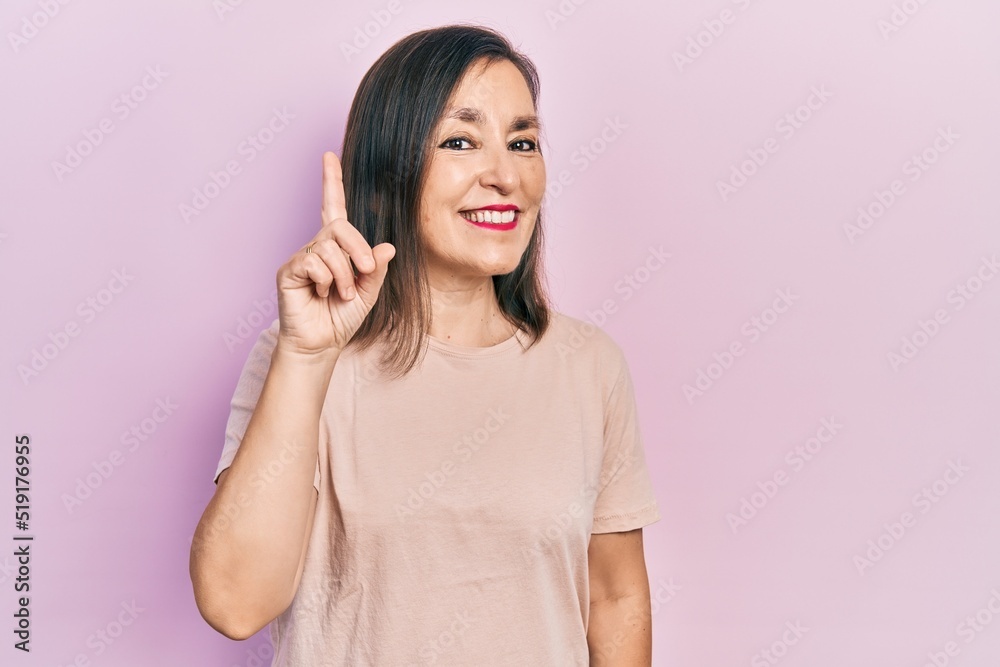 Middle age hispanic woman wearing casual clothes showing and pointing up with finger number one while smiling confident and happy. Middle age hispanic woman wearing casual clothes showing and pointing up with finger number one while smiling confident and happy.