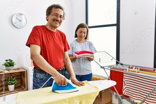 Middle age man and woman couple smiling confident ironing clothes at laundry