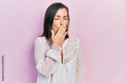 Middle age hispanic woman wearing casual clothes bored yawning tired covering mouth with hand. restless and sleepiness.
