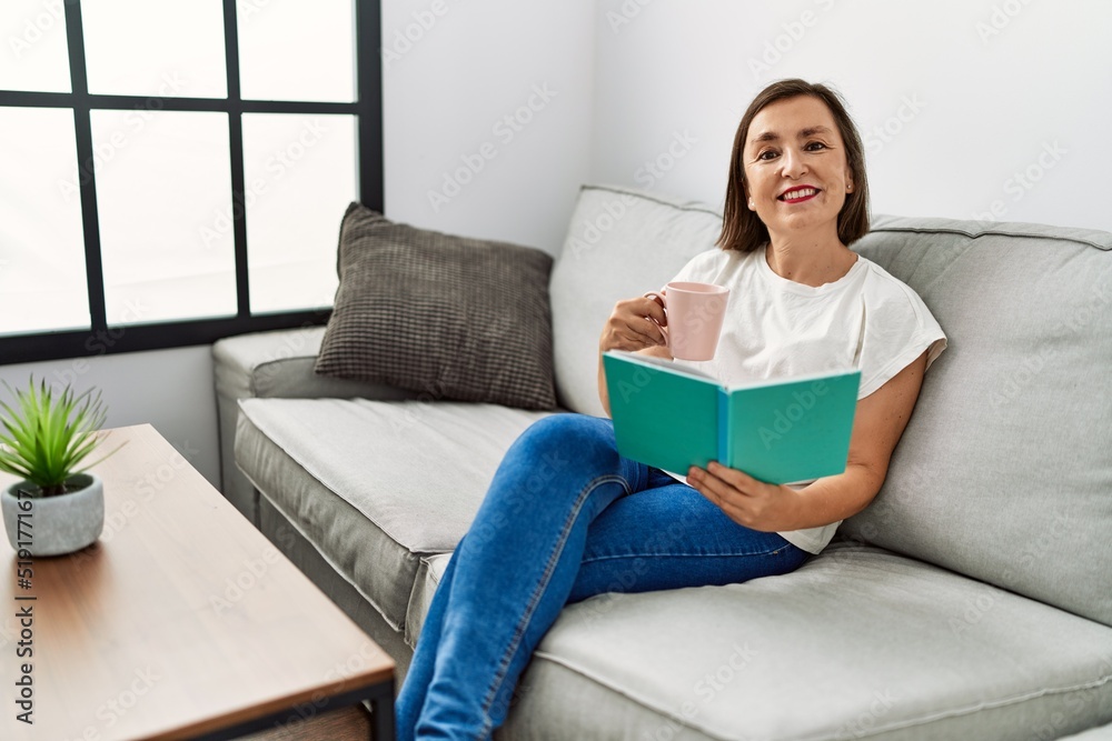 Middle age hispanic woman smiling sitting on the sofa reading a book at home Middle age hispanic woman smiling sitting on the sofa reading a book at home