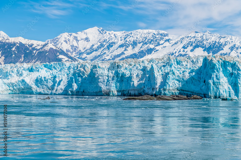 A view past an islet towards the snout of the Hubbard Glacier with mountain backdrop in Alaska in summertime