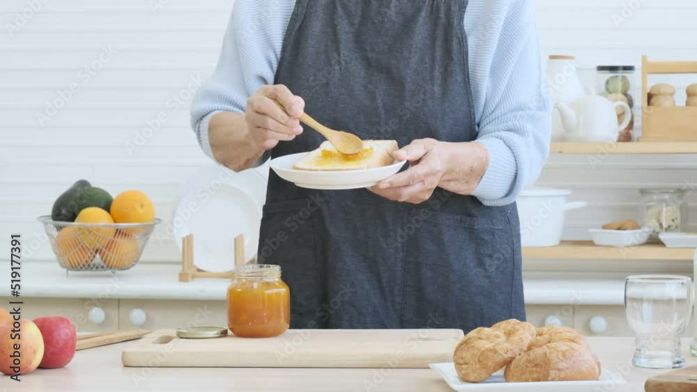 Elderly woman spreading bread with marmalade in the kitchen. Elderly woman spreading bread with marmalade in the kitchen.
