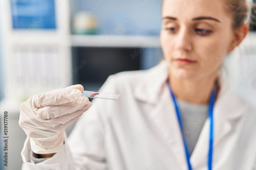 Young blonde woman wearing scientist uniform analysing blood at laboratory Young blonde woman wearing scientist uniform analysing blood at laboratory