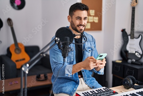Young hispanic man artist smiling confident using smartphone at music studio