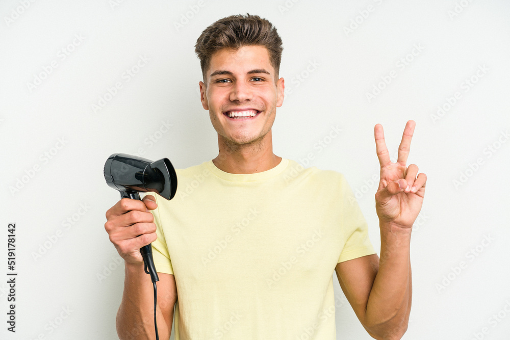 Young caucasian man holding hairdryer isolated on white background showing number two with fingers. Young caucasian man holding hairdryer isolated on white background showing number two with fingers.
