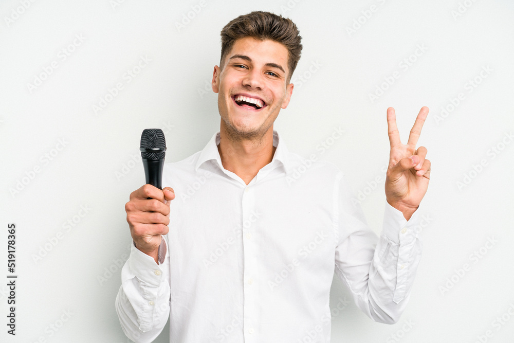 Young singer caucasian man isolated on white background joyful and carefree showing a peace symbol with fingers. Young singer caucasian man isolated on white background joyful and carefree showing a peace symbol with fingers.
