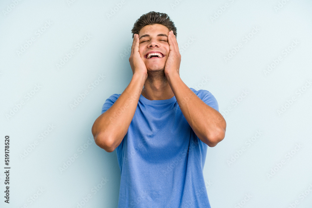 Young caucasian man isolated on blue background laughs joyfully keeping hands on head. Happiness concept. Young caucasian man isolated on blue background laughs joyfully keeping hands on head. Happiness concept.