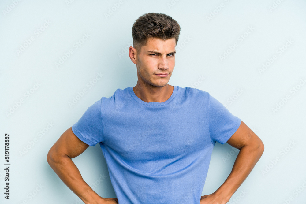Young caucasian man isolated on blue background frowning face in displeasure, keeps arms folded. Young caucasian man isolated on blue background frowning face in displeasure, keeps arms folded.
