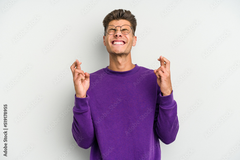 Young caucasian man isolated on white background crossing fingers for having luck