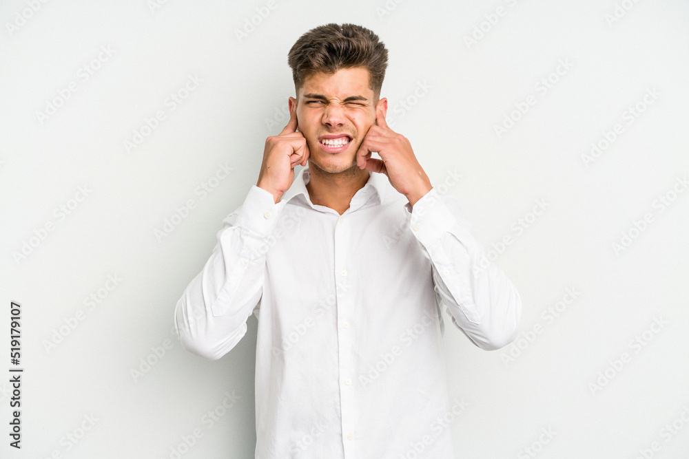 Young caucasian man isolated on white background covering ears with fingers, stressed and desperate by a loudly ambient. Young caucasian man isolated on white background covering ears with fingers, stressed and desperate by a loudly ambient.