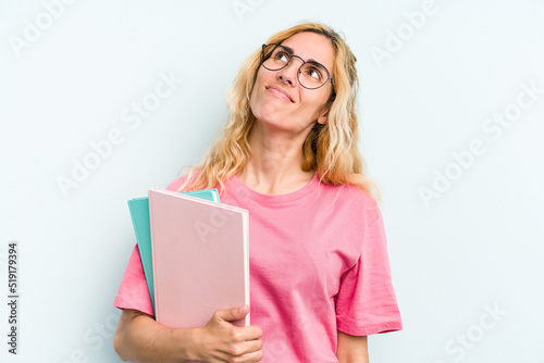 Young student caucasian woman holding books isolated on blue background dreaming of achieving goals and purposes