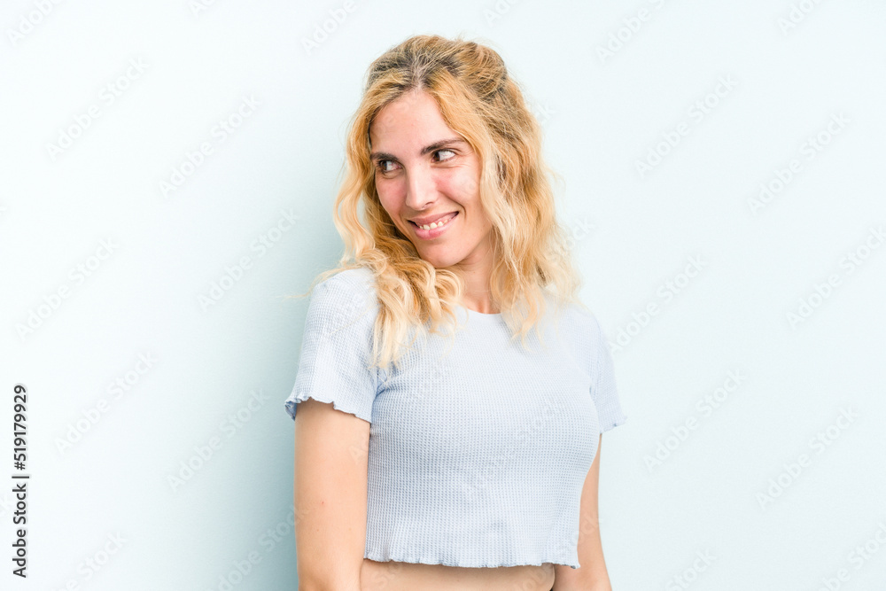 Young caucasian woman isolated on blue background looks aside smiling, cheerful and pleasant.