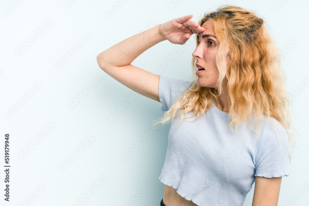 Young caucasian woman isolated on blue background looking far away keeping hand on forehead. Young caucasian woman isolated on blue background looking far away keeping hand on forehead.
