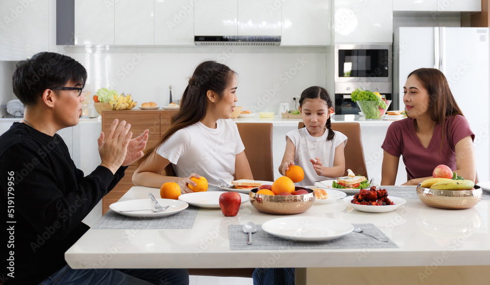 A large, happy Asian family spends time dining at a table in their home. Cute little daughter having fun chatting. A large, happy Asian family spends time dining at a table in their home. Cute little daughter having fun chatting.