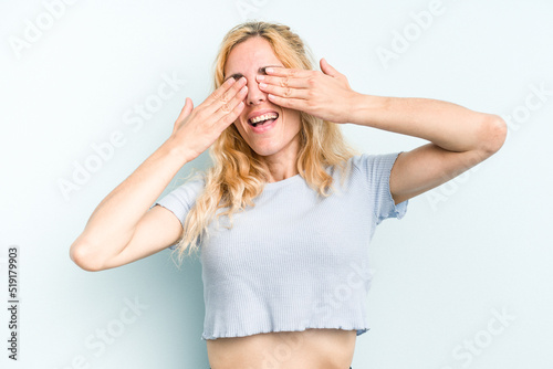 Young caucasian woman isolated on blue background covers eyes with hands, smiles broadly waiting for a surprise.