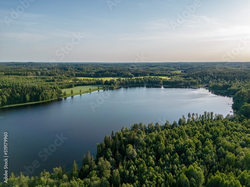 Aerial view of beautiful lake at summertime in Finland. Forest surrounding the lake a few fields on the background.