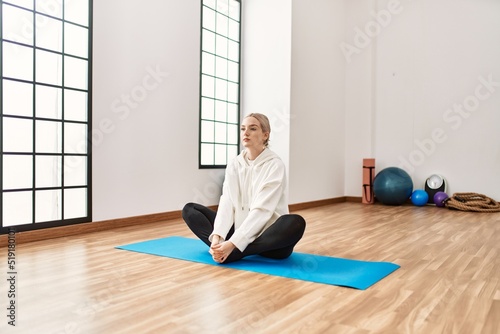 Young blonde girl concentrated stretching at sport center.