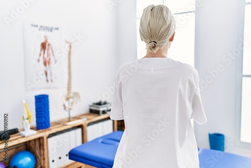 Young caucasian woman working at pain recovery clinic standing backwards looking away with crossed arms