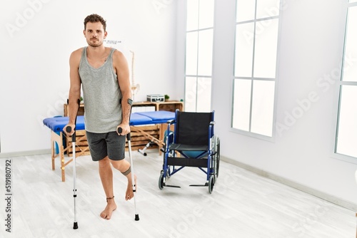 Young hispanic man walking using crutches at clinic