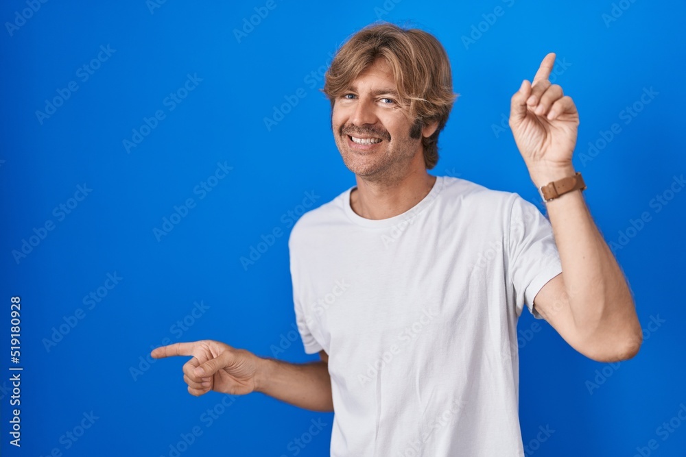 Middle age man standing over blue background smiling confident pointing with fingers to different directions. copy space for advertisement Middle age man standing over blue background smiling confident pointing with fingers to different directions. copy space for advertisement