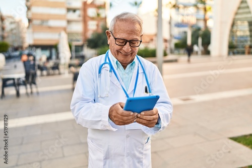 Senior man wearing doctor uniform using touchpad at street © Krakenimages.com