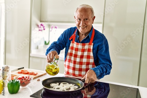 Senior man smiling confident pouring oil on frying pan at kitchen