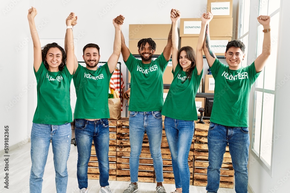 Obraz premium Group of young volunteers smiling happy with hands raised up at charity center.