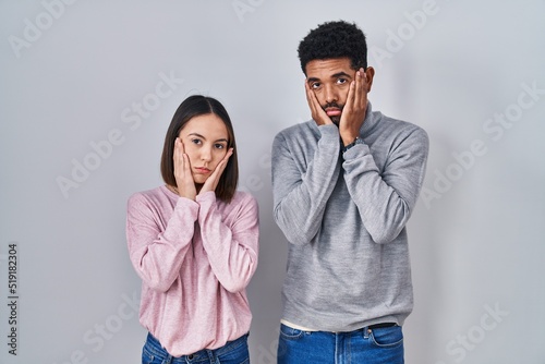 Young hispanic couple standing together tired hands covering face, depression and sadness, upset and irritated for problem