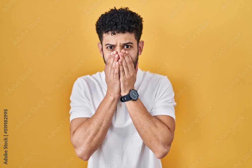 Arab man standing over yellow background shocked covering mouth with hands for mistake. secret concept. Arab man standing over yellow background shocked covering mouth with hands for mistake. secret concept.