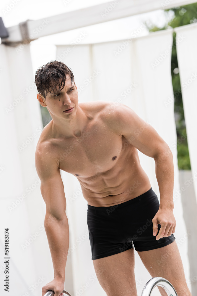 Obraz premium wet man with sportive body standing near pool ladder.