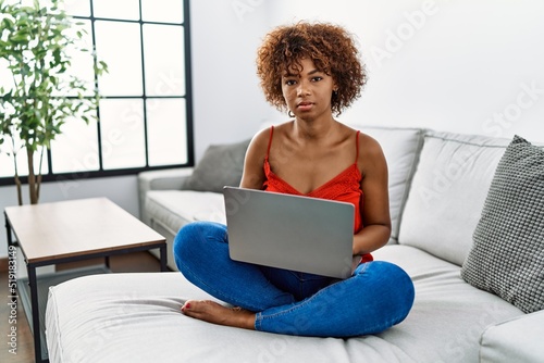 Young african american woman sitting on the sofa at home using laptop skeptic and nervous, frowning upset because of problem. negative person.
