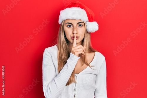 Beautiful hispanic woman wearing christmas hat asking to be quiet with finger on lips. silence and secret concept.