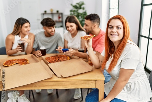Group of young people smiling happy eating italian pizza sitting on the table at home