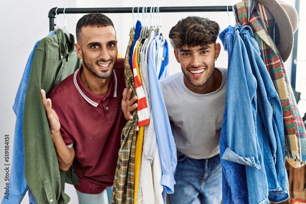 Young hispanic man smiling happy appearing through clothes at clothing store.