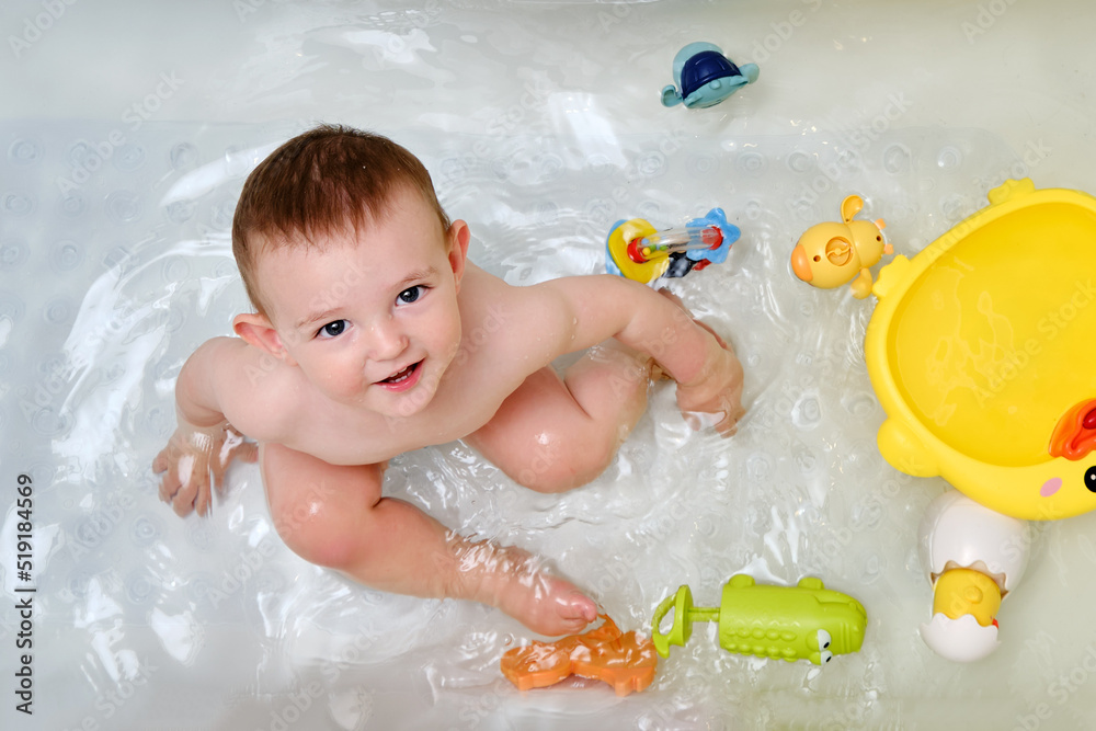 Happy toddler baby boy is playing with toys in the bathtub. A smiling child plays in the water of a home bathroom Happy toddler baby boy is playing with toys in the bathtub. A smiling child plays in the water of a home bathroom